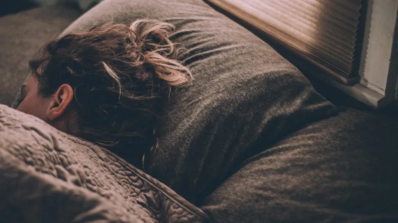 a person sleeps on brown bedding. only their head can be seen protruding from the covers