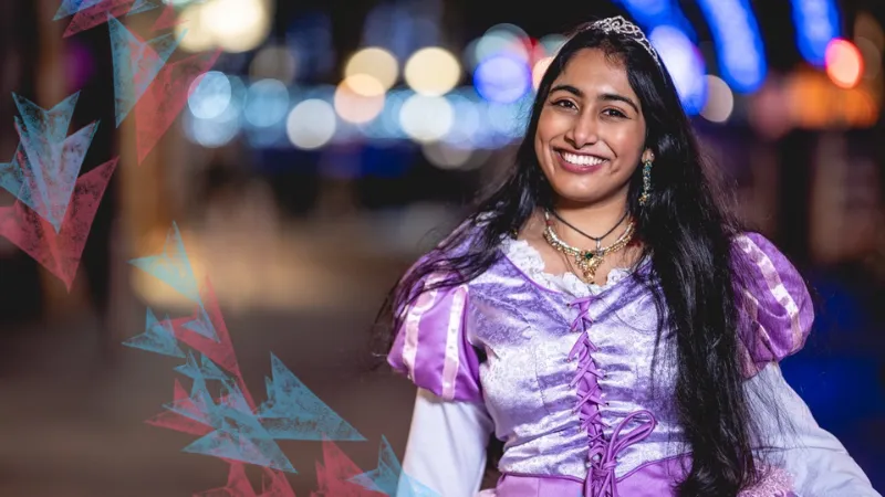 Soamopriya wearing a purple princess dress and crown smiling at the camera