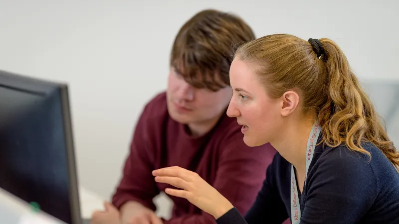 A student and a member of staff collaborating in front of a computer screen.