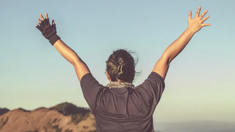 a person stands at the top of a long hike with their arms outstretched towards the sky