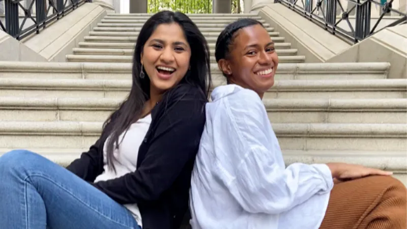 Amna and Rianna sitting on the Bush House courtyard steps smiling at the camera