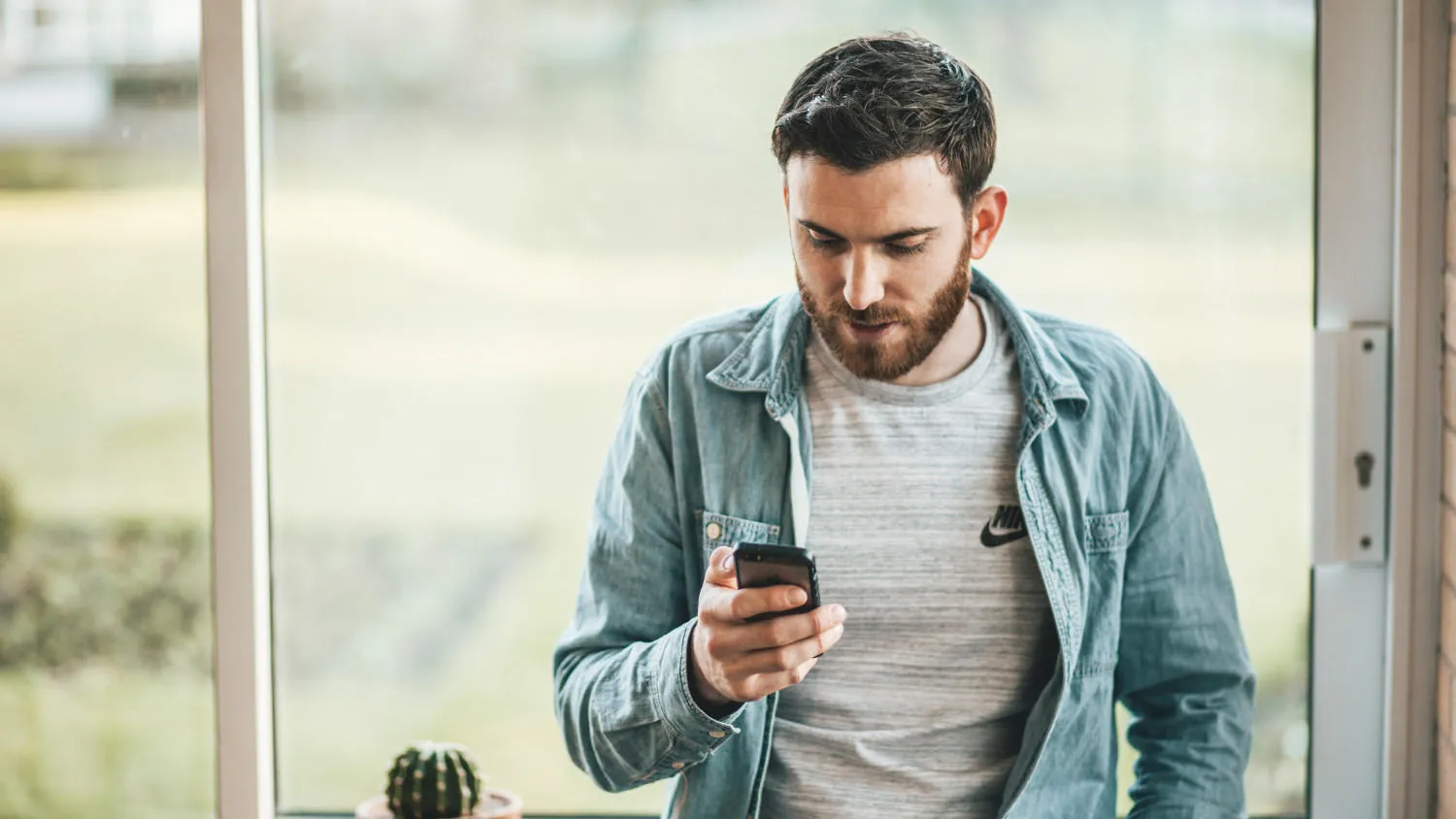 a student leans against a window while looking at their phone