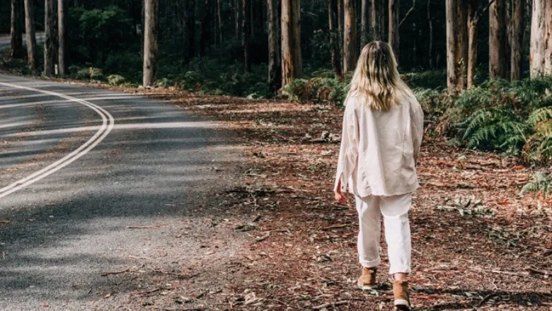 Woman walking on the outskirts of a wood next to an empty road