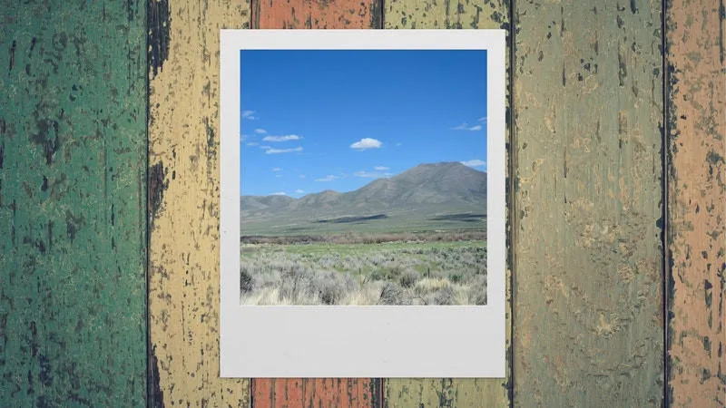 A polaroid picture depicting an arid and rocky desert landscape lays on top of colourful wooden boards