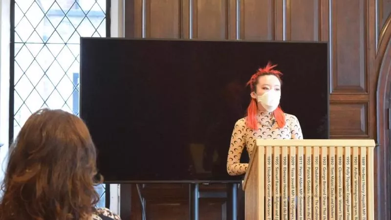 a young person speaks from behind a podium in a wood panelled room