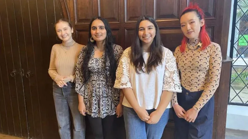 four young people stand shoulder to shoulder in front of a wood panelled wall