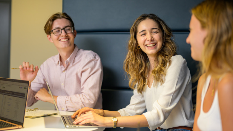 Three students talking and laughing while working on a group project