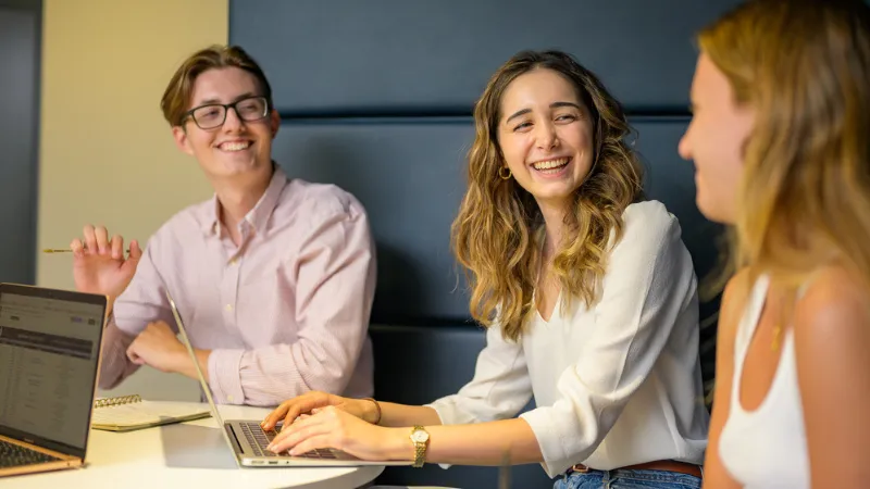 Three students talking and laughing while working on a group project