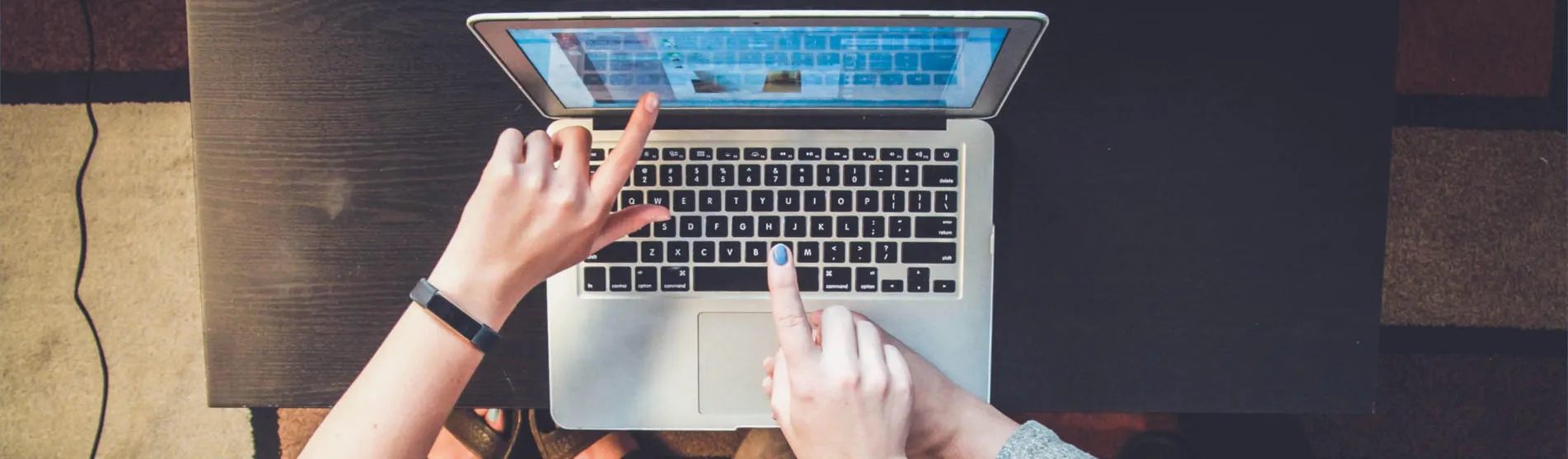 three hands point at the screen of a laptop