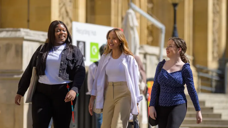 Three students walking by the Maughan Library talking and laughing