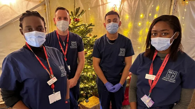 a group of healthcare professionals in scrubs and face coverings stand in front of a Christmas tree