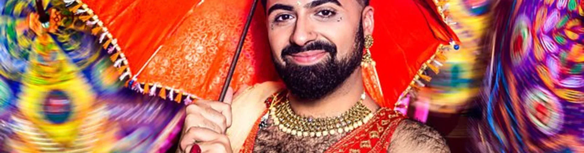 Vinay wearing an Indian vest and holding a red umbrella in front of a background of colourful umbrellas.