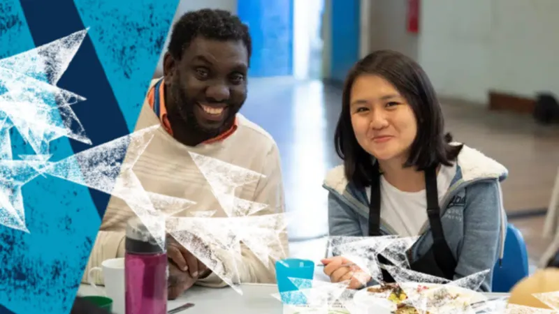 Two students sitting at a table and smiling to the camera.