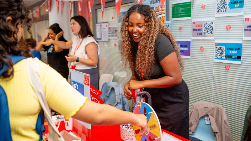 King's student spinning a wheel to win a prize at the King's Welcome Hub, with smiling member of staff.
