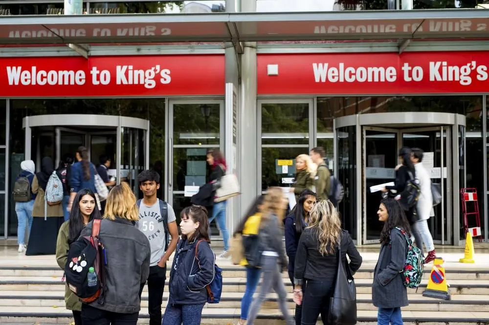 Students gather in groups outside a King's building. Signs reading "Welcome to King's" are hung above two revolving doors