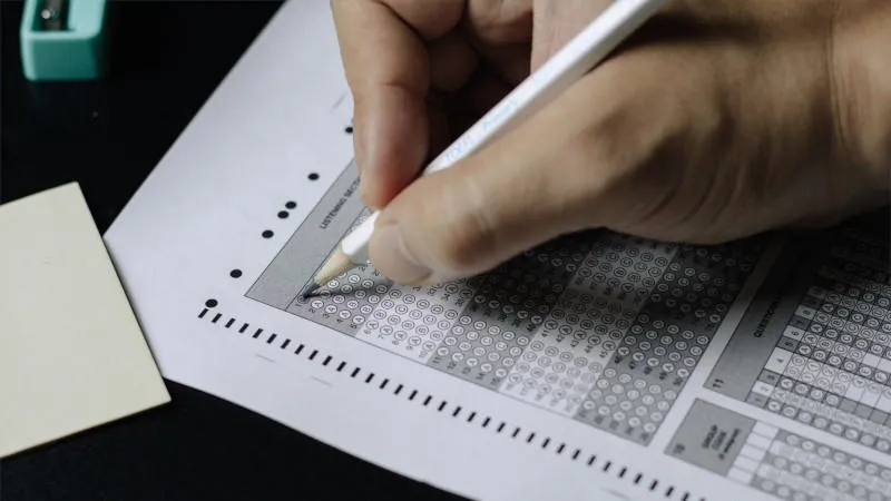 A hand holding a pencil fills out a multiple choice exam answer paper