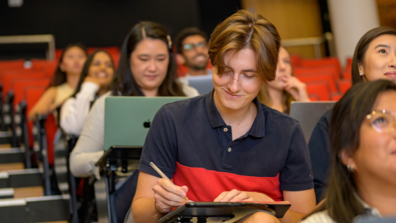 student-writing-notes-in-lecture-theatre-thumbnail-promo-aug-2022-780-x-440-pixels