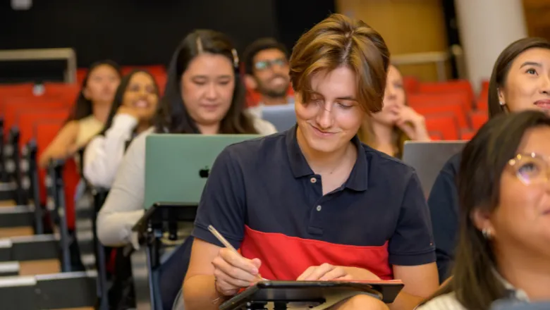 student-writing-notes-in-lecture-theatre-thumbnail-promo-aug-2022-780-x-440-pixels