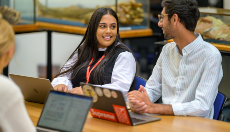 Three students working on laptops, in conversation 