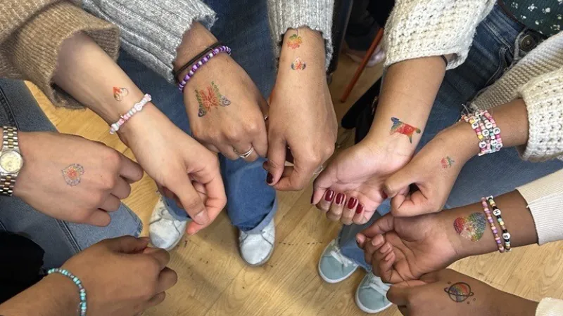 A group shows off colorful temporary tattoos and beaded bracelets on their hands and wrists.