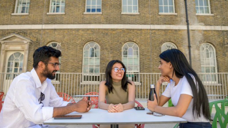 Three students sit at a table talking