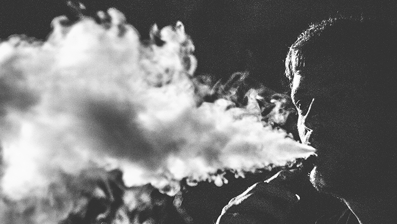black and white image of man exhaling thick white vape smoke