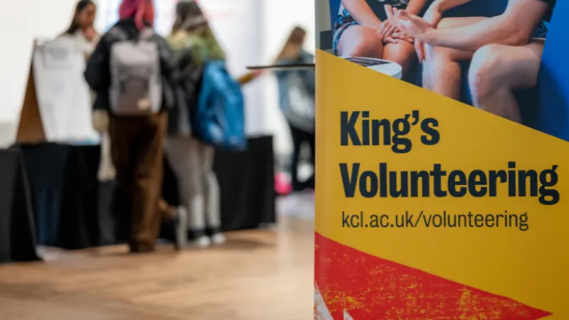 Three students speaking to a staff member at a volunteering stall in the background. On the right hand side of the image 