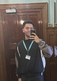 Altug Yamak wears a black and grey jumper and is holding a phone 