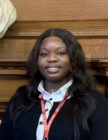 Sharon Adebola smiles and wears a black and white cardigan.